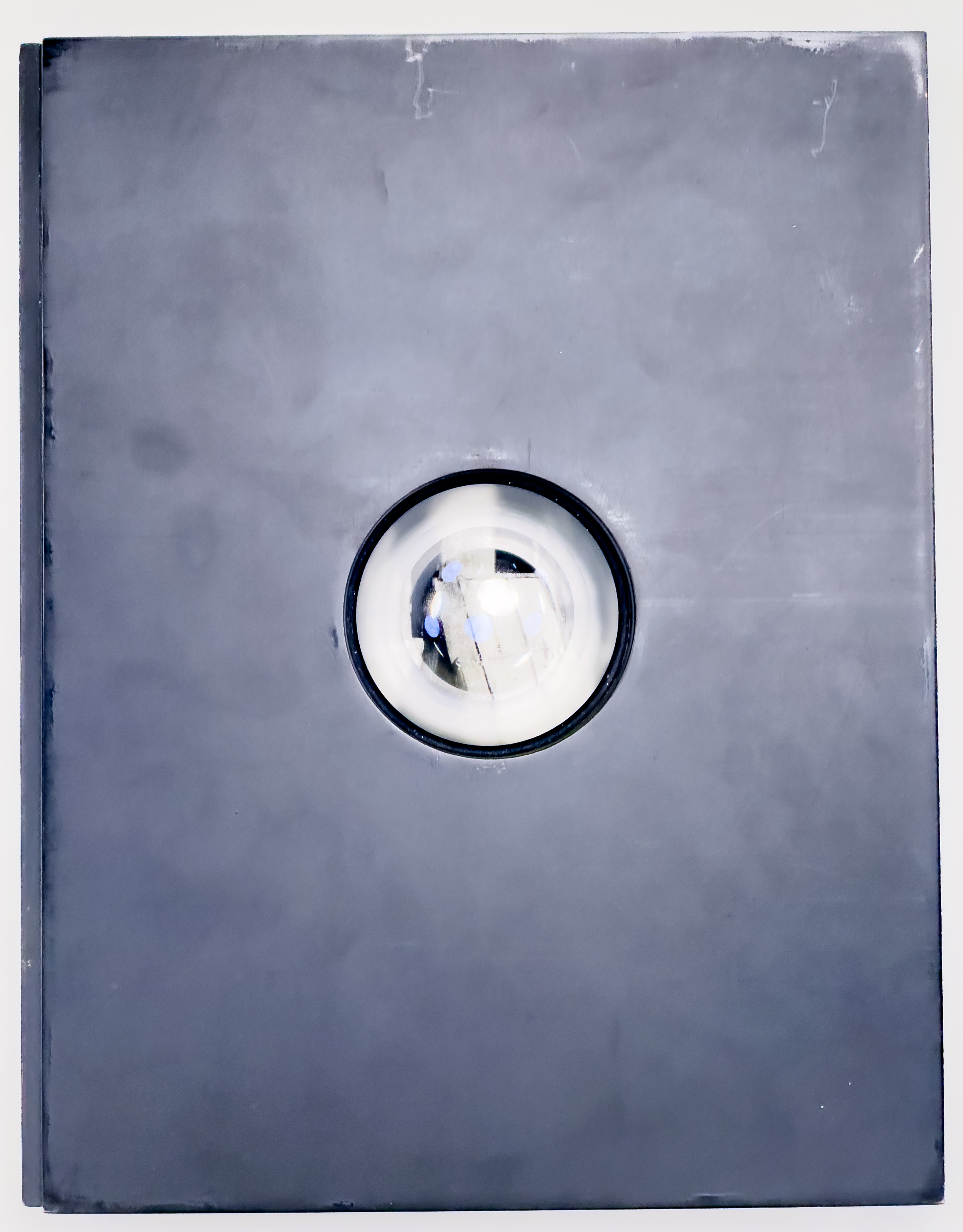 Black book cover with a circular cut out in the center with a glass lens inside.