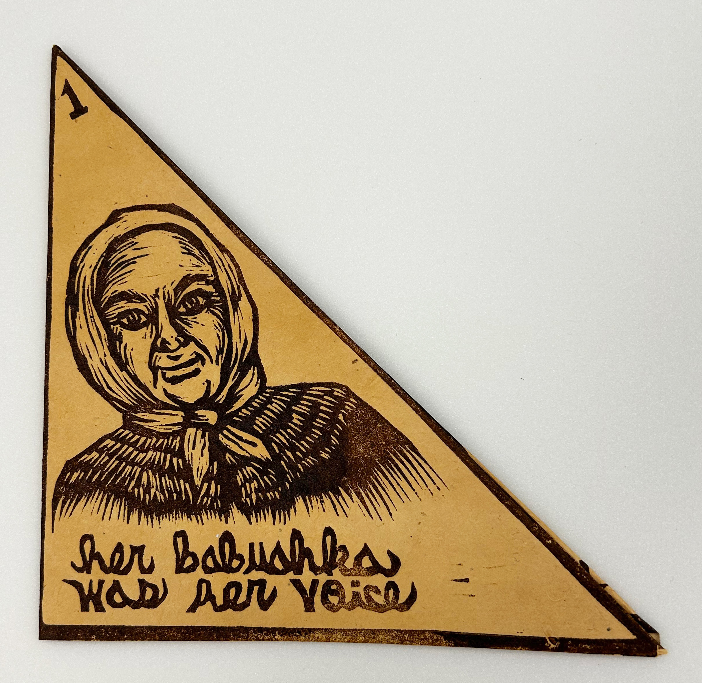 A linoleum block print folded into a book with a black relief print of an old woman in a head scarf on the brown cover with the title in black, "Her Babushka Was Her Voice," at the bottom. 