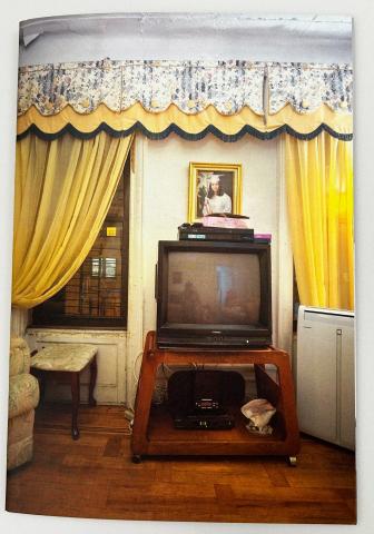 Colored photograph of a vintage living room with a Box TV and a graduation picture of a woman on the wall